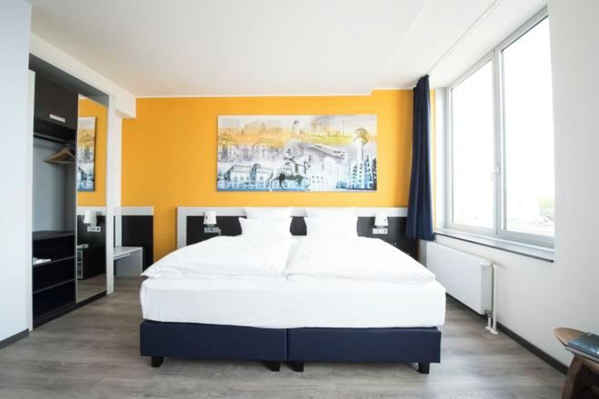 Ein Hotelzimmer mit Bett, einem Bild an der Wand, einem Fenster und einem Schreibtisch.
