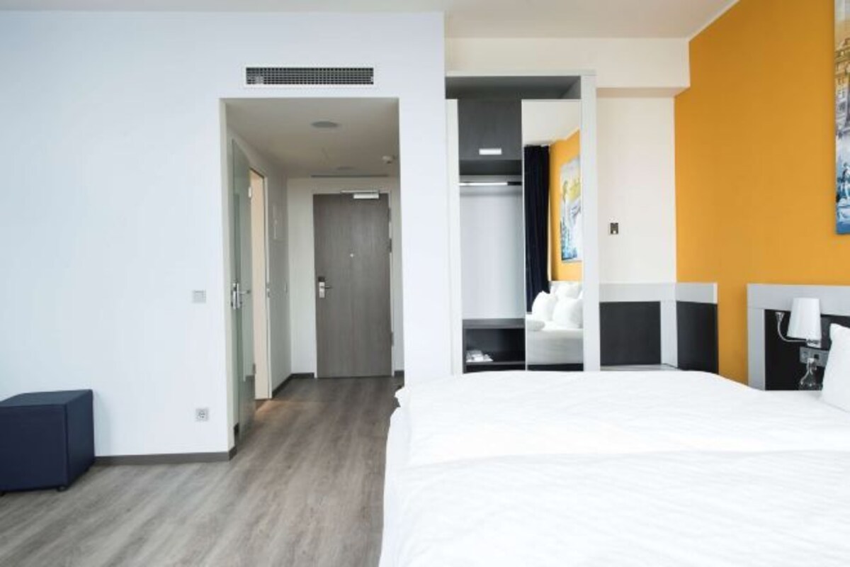 Ein Hotelzimmer mit einem großen Bett, einem Kleiderschrank und einem durch eine geöffnete Tür einsehbarer Badezimmer.
