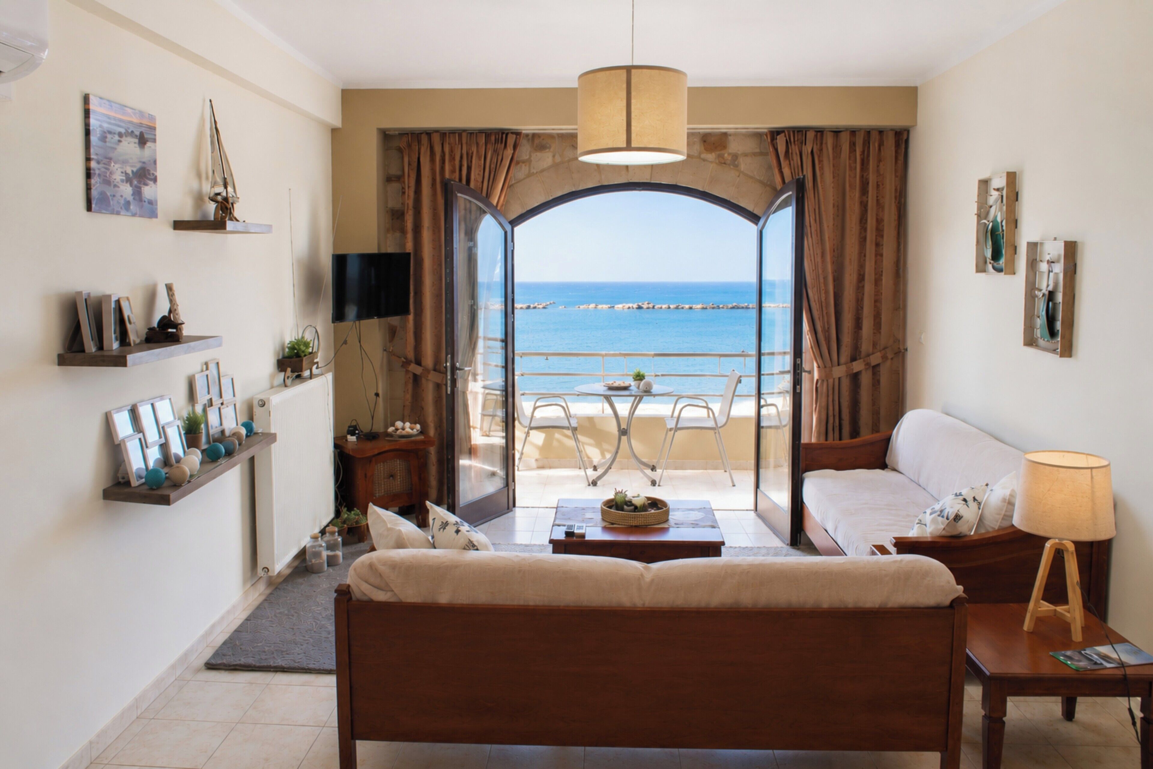 A room with a bed, a sofa, a coffee table, and a view of the sea through an open archway.