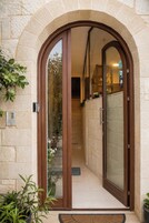 Una entrada arqueada con puerta corredera de vidrio, pared de piedra y plantas en macetas.