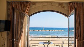 A room with a view of the beach, a table with a basket, a sofa, and a television on the wall.