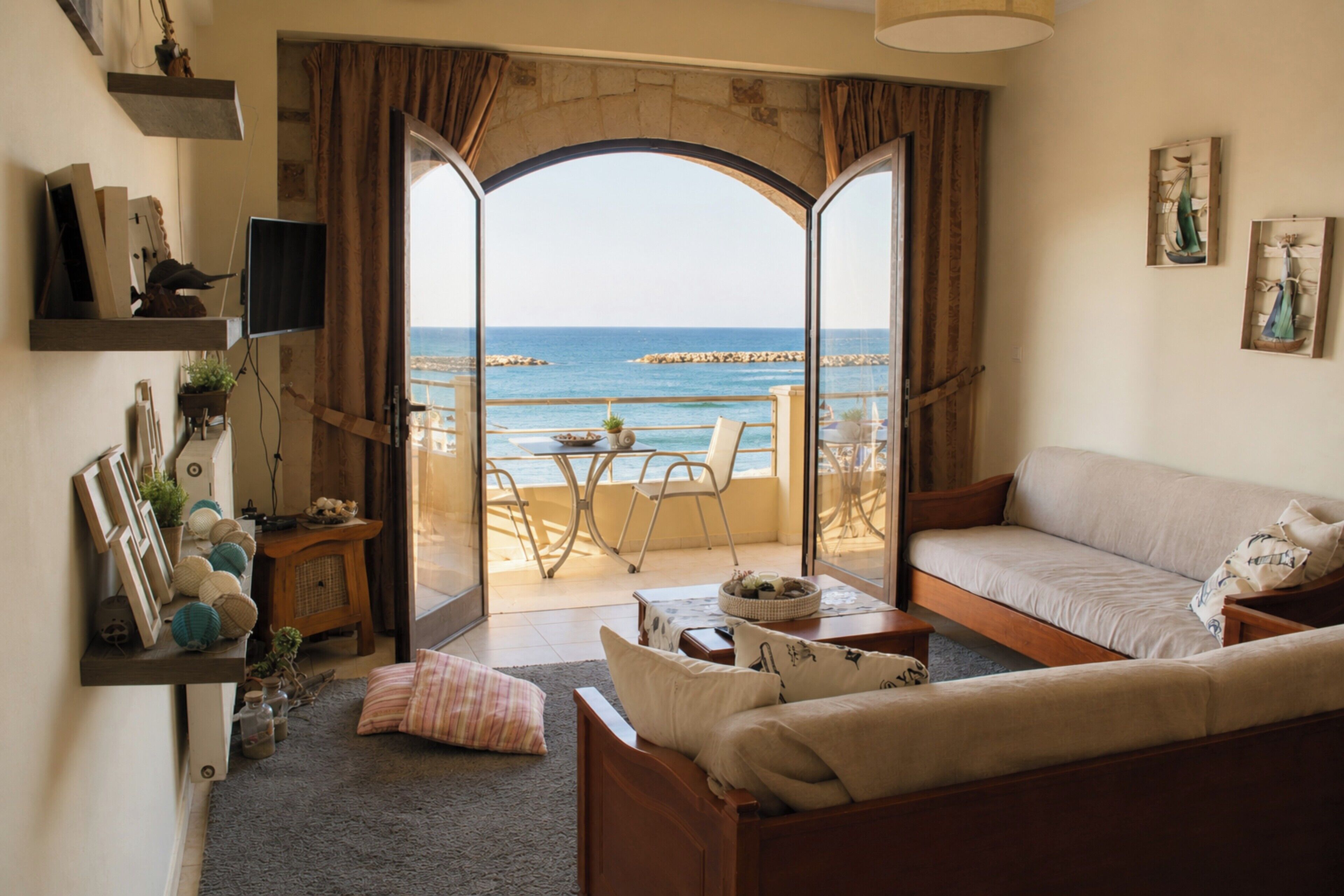 A living room with a sofa, a coffee table, a TV, and a view of the sea through a glass door.