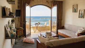 A living room with a sofa, a coffee table, a TV, and a view of the sea through a glass door.