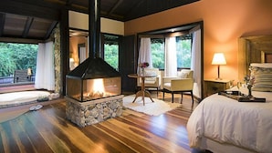 Una habitación acogedora con chimenea de piedra, una cama, una zona de estar con una mesa y vistas al exterior.