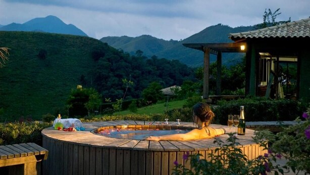Un jacuzzi con muelle de madera, rodeado de exuberante vegetación y colinas al fondo.