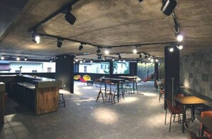 Un interior con una zona de bar, mesas, sillas y una escalera que lleva a un nivel superior.