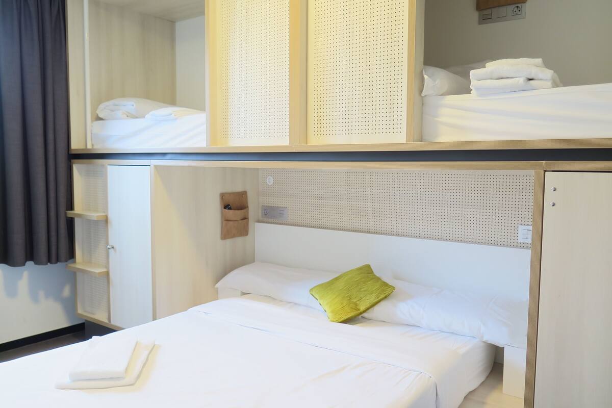 A hotel room with a bunk bed, a single bed, and a small storage unit with shelves.