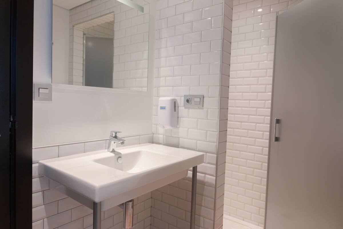 A modern bathroom with white subway tiles, a white sink, a mirror, and a soap dispenser.