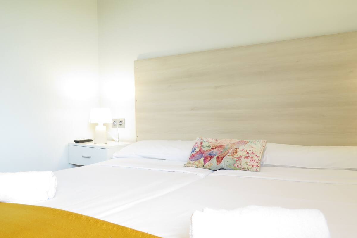 A neatly made bed with a floral pillow, a bedside table with a lamp, and a yellow blanket.