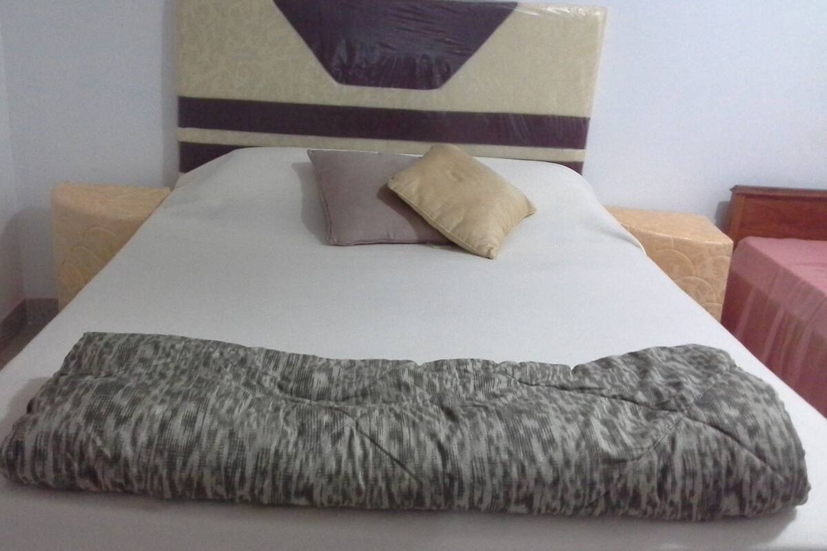 A bed with a headboard, two pillows, a blanket, and a wooden nightstand.