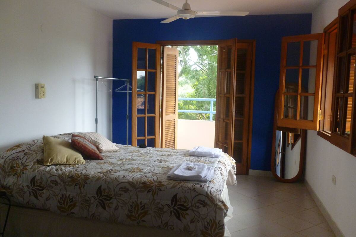 A bedroom with a bed, a ceiling fan, and a view of the outside through open doors.