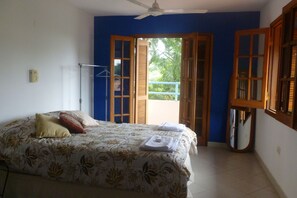 Un dormitorio con cama, ventilador de techo y vistas al exterior a través de puertas abiertas.