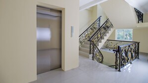 A modern interior with a metallic elevator, a staircase with ornate black railings, and a spacious hallway. - RedDoorz Plus @ Cideng Barat (Jakarta)