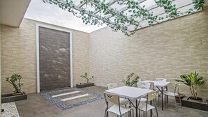 A modern patio area with a brick wall, a glass door, and a seating arrangement with tables and chairs. - RedDoorz Plus @ Cideng Barat (Jakarta)