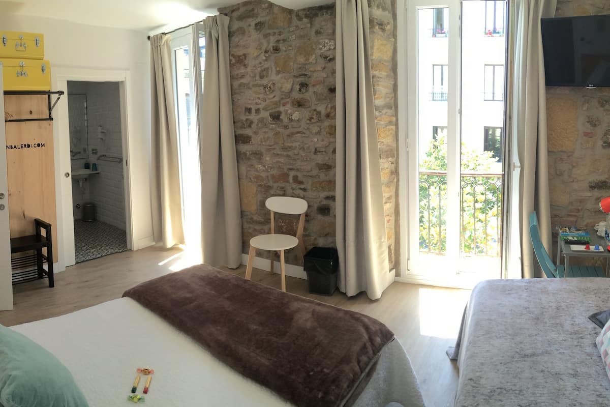 A hotel room with a stone wall, a bed with a brown blanket, a sofa with patterned cushions, a small table, and a TV mounted on the wall.