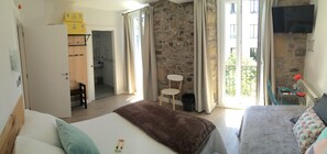 Una habitación de hotel con pared de piedra, una cama con manta marrón, un sofá con cojines estampados, una mesita y un televisor montado en la pared.