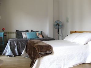A bedroom with a bed, a bedside table, a chair, a standing fan, and a radiator. - Pension Balerdi (San Sebastián)