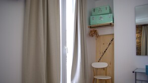 A room with a wooden chair, a small table, and a trash bin. There are two green suitcases on a shelf above the door. - Pension Balerdi (San Sebastián)