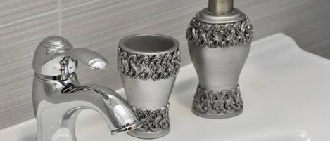 A bathroom sink with a chrome faucet, a decorative glass cup, and a soap dispenser.