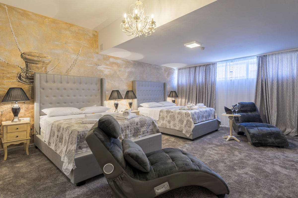 Een moderne hotelkamer met twee bedden, een massagestoel en een kroonluchter.