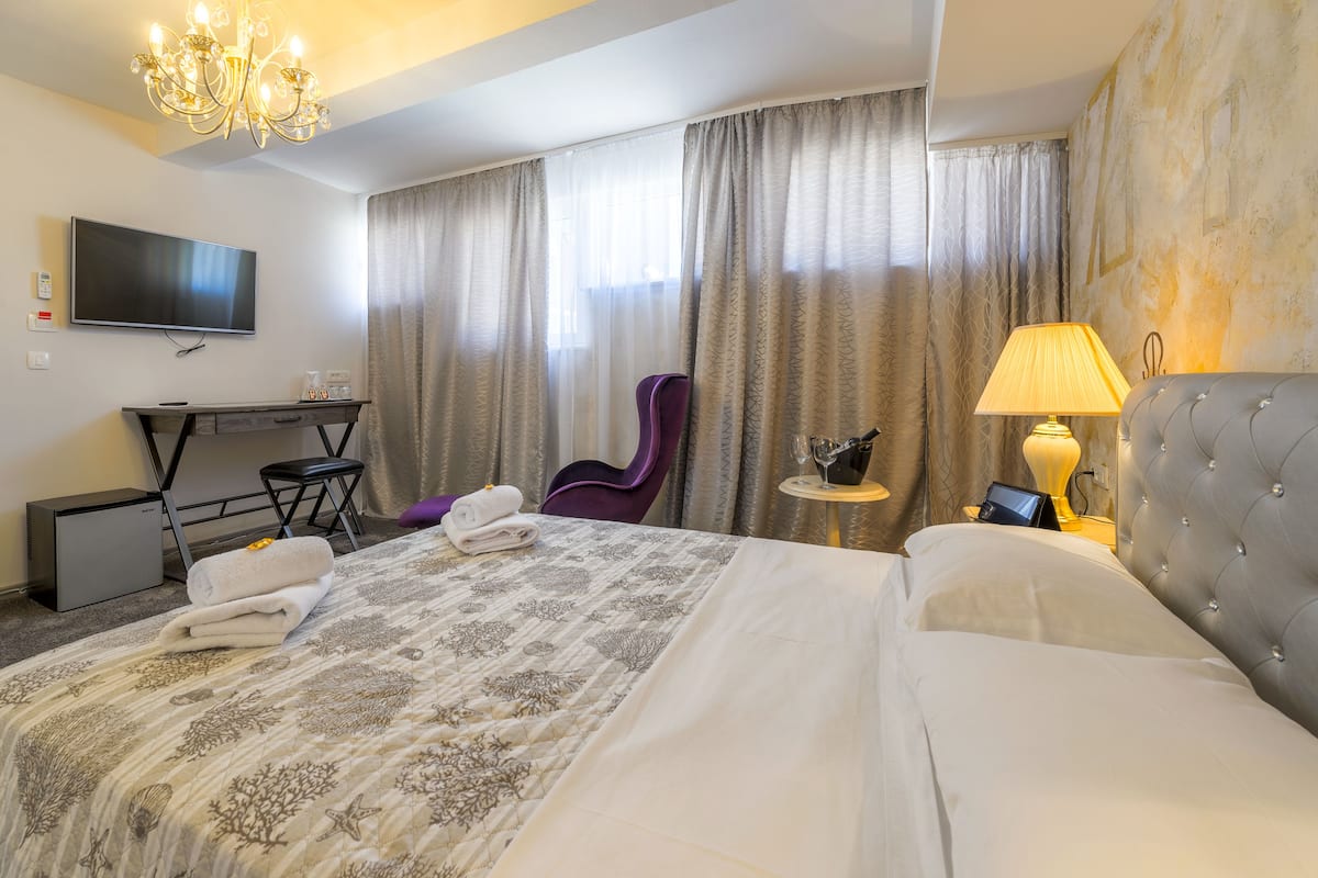 Hotelkamer met een groot bed, een bureau met een flatscreen televisie, een stoel, een lamp en een klein tafeltje met een wijnglas.