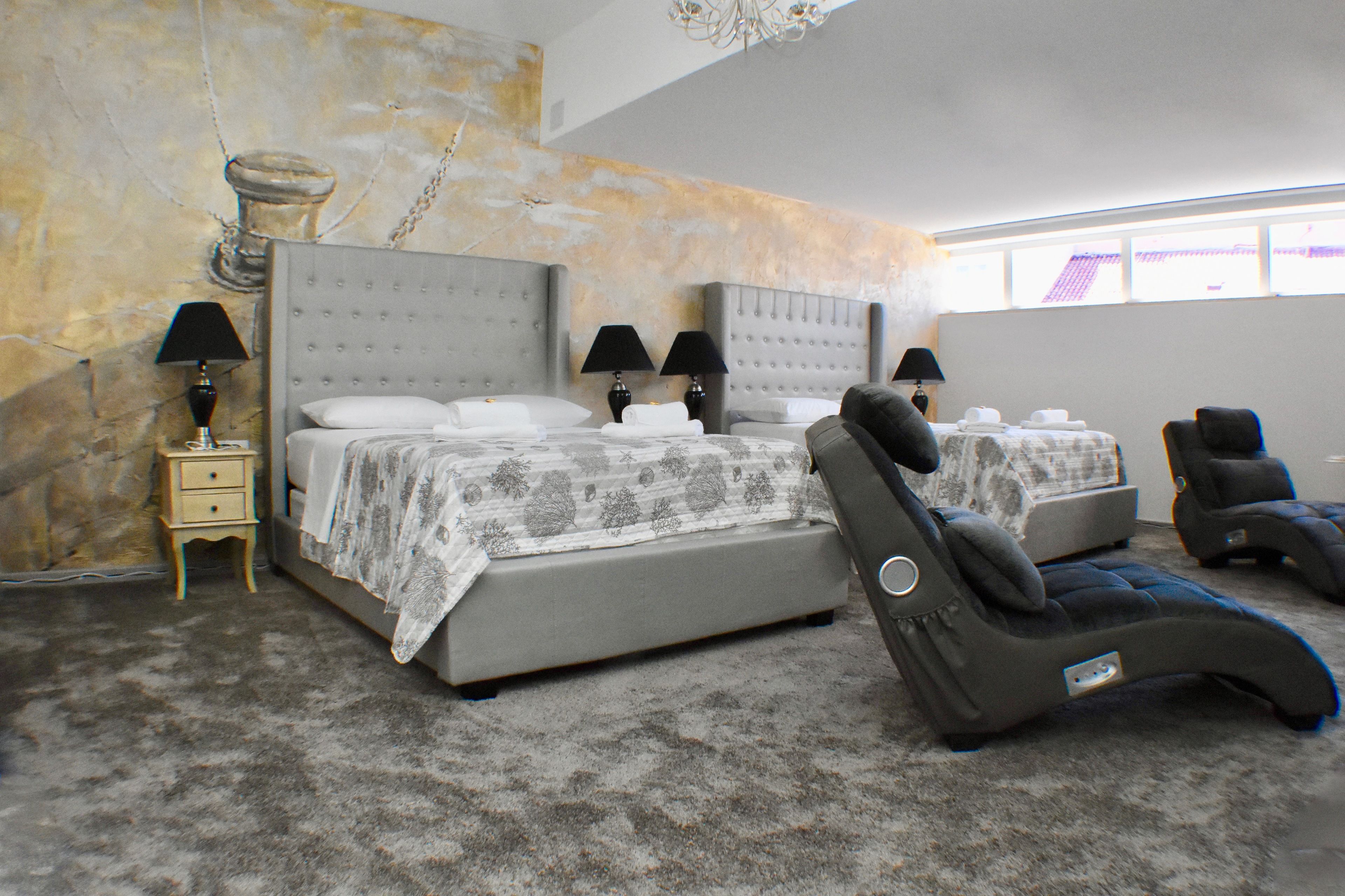 Une chambre dotée d’un grand lit, de deux tables de chevet avec des lampes, d’un fauteuil de massage et offrant une vue sur l’extérieur par une fenêtre.