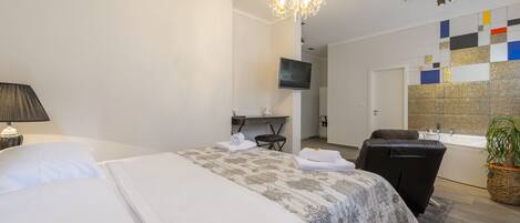 A hotel room with a large bed, a desk with a chair, a TV, a massage chair, and a bathtub.