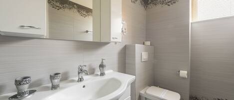 A bathroom with a white sink, two decorative cups, a mirror, a toilet, and a shower area.