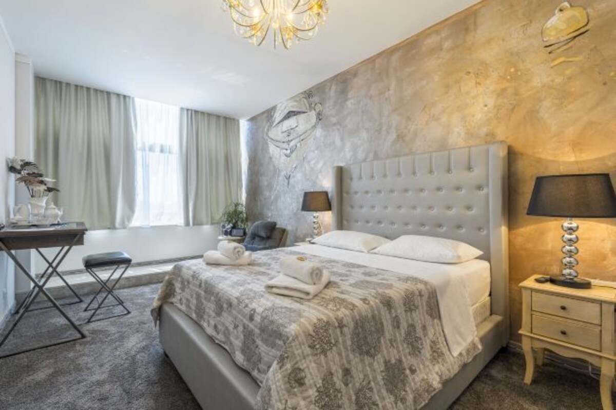Habitación de hotel con una cama grande, mesitas de noche, un escritorio y una ventana con cortinas.