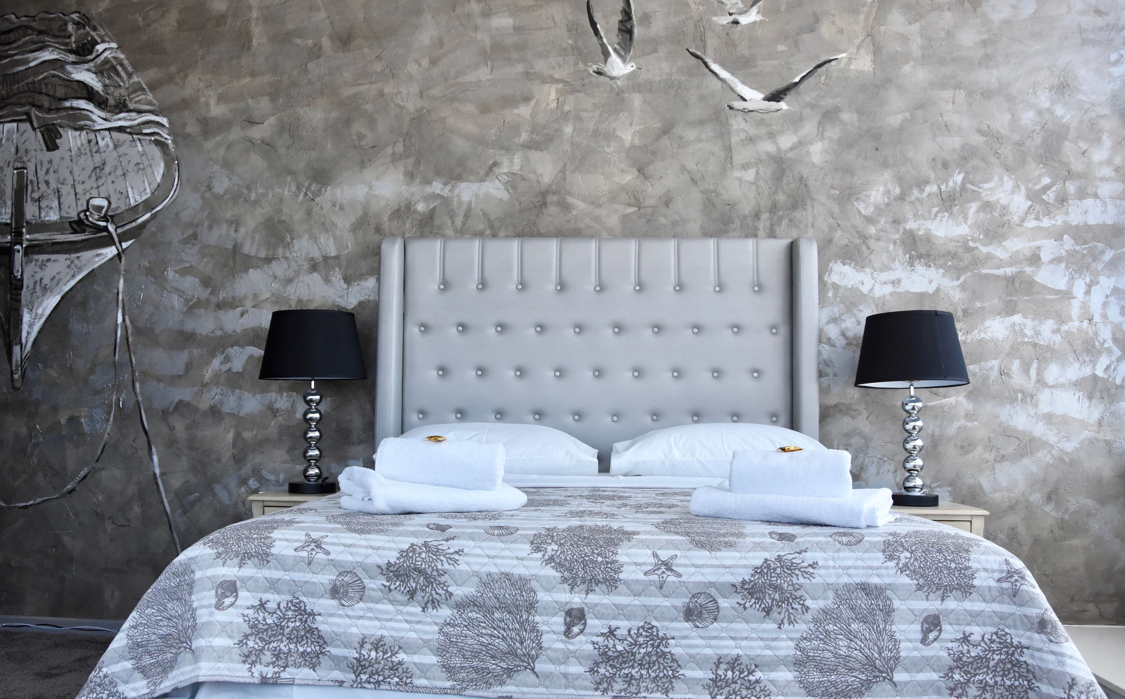 A bedroom with a tufted headboard, two bedside tables with lamps, a bed with a patterned bedspread, and a wall with a textured surface and a decorative wall hanging.