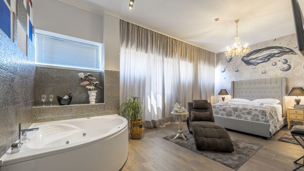 Een moderne slaapkamer met een ruime badkuip, een comfortabele bank, een bed met een grijze hoofdbord en een wanddecoratie.