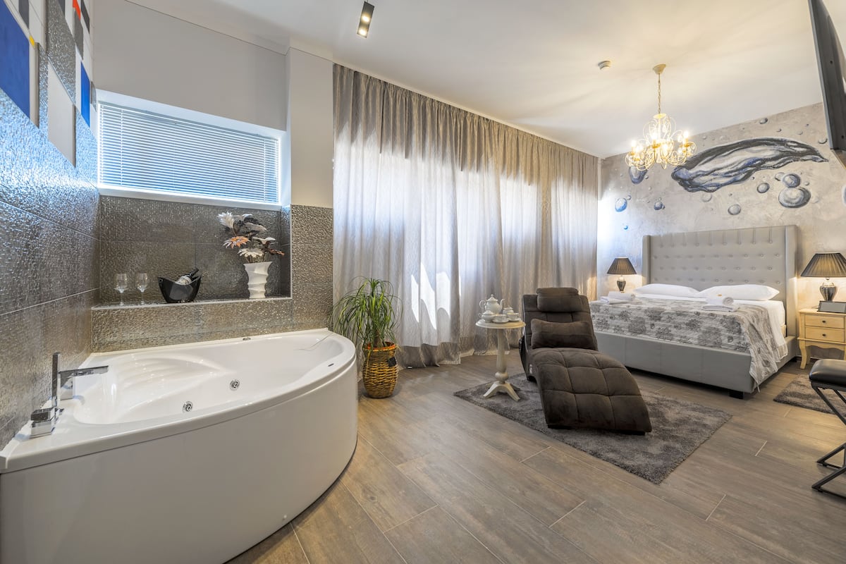 Een moderne slaapkamer met een ruime badkuip, een comfortabele bank, een bed met een grijze hoofdbord en een wanddecoratie.
