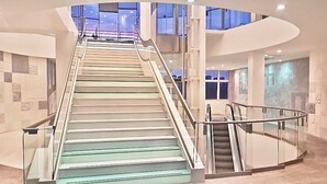 Een modern interieur met een centrale trap, glazen balustrades en een gebogen plafond.