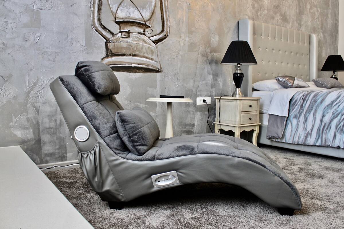 Een massagestoel in een kamer met een bed, nachtkastjes en een wandlamp.