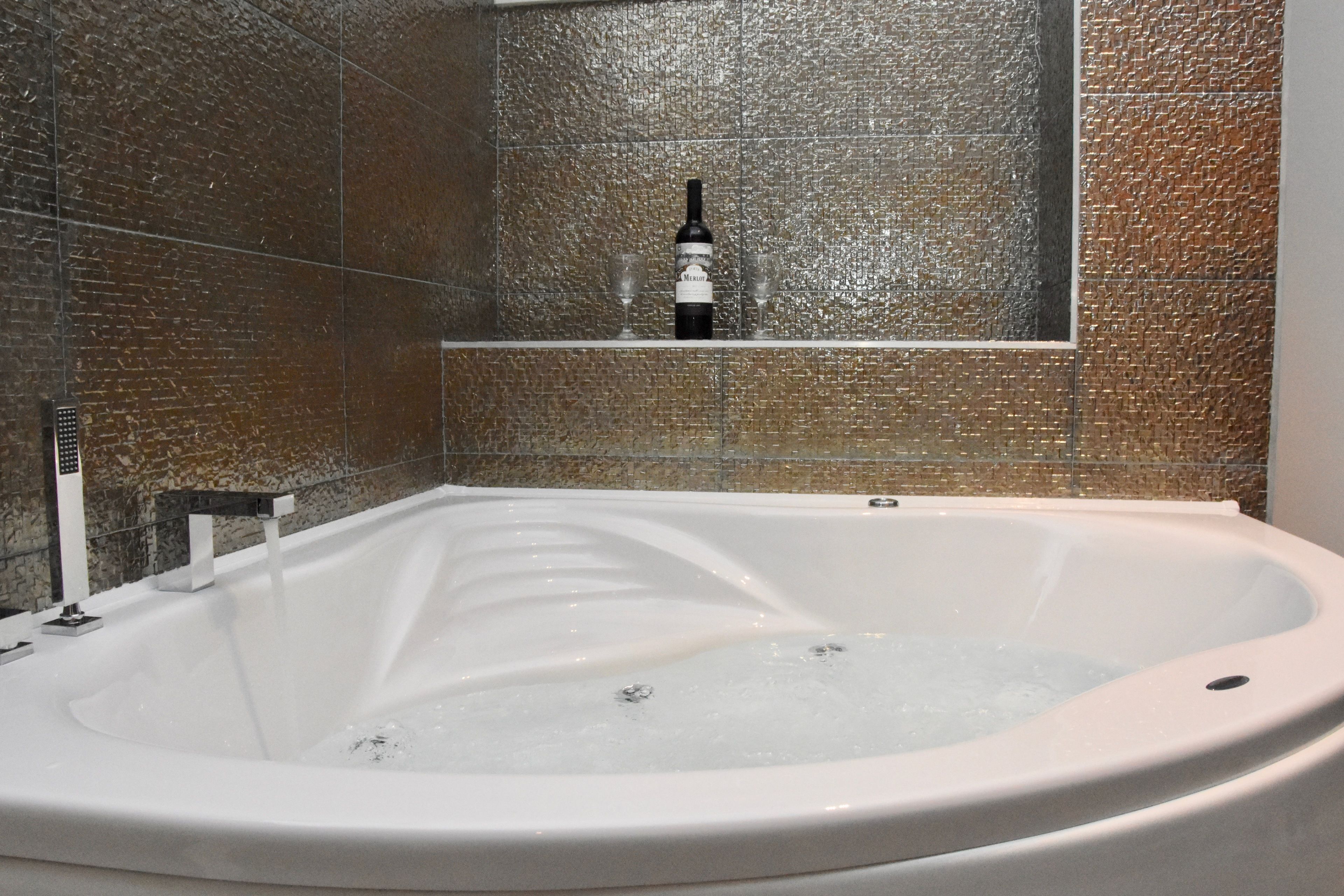 Une salle de bain moderne avec une baignoire sur pieds, une étagère en verre avec une bouteille et des verres, et un mur à texture.