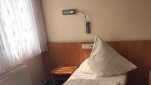 A single bed with a wooden headboard, a bedside table, and a wall-mounted lamp. - Hotel Montan (Duisburg)