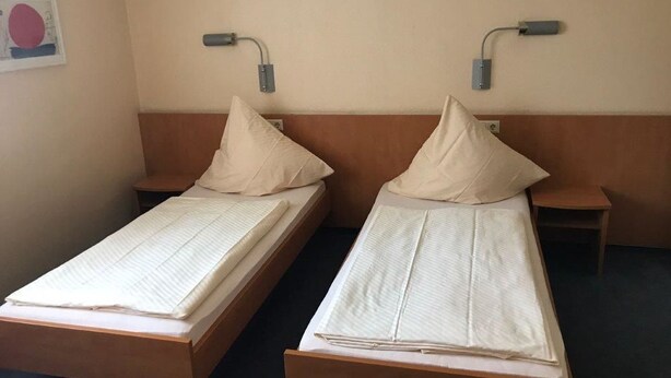 Two single beds with wooden frames and headboards, each with a pillow and a bedside table. - Hotel Montan (Duisburg)
