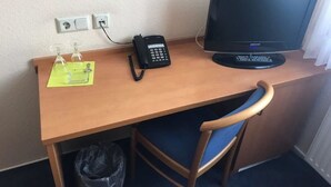A wooden desk with a computer monitor, a telephone, and a chair. - Hotel Montan (Duisburg)