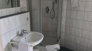 A bathroom with a white sink, mirror, and toilet. It includes a shower area with a glass door and a towel hanging on the wall. - Hotel Montan (Duisburg)