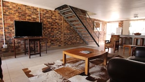 A living room with a brick wall, a TV on a stand, a wooden coffee table, a leather sofa, a cowhide rug, and a staircase. - Clanwilliam Accommodation (Cederberg)