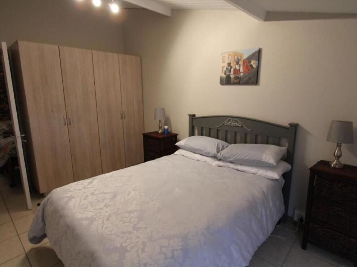 Un dormitorio con una cama grande, un armario, una mesita de noche con una lámpara y un cuadro en la pared.