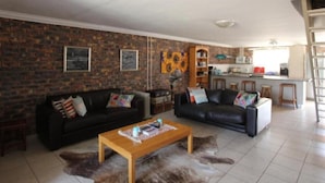 A living room with two black leather sofas, a wooden coffee table, and a brick wall. - Clanwilliam Accommodation (Cederberg)