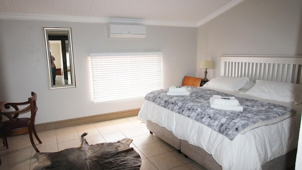 A bedroom with a bed, a chair, a window with blinds, a mirror, and a radiator. - Clanwilliam Accommodation (Cederberg)