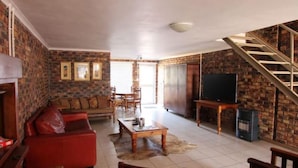 A living room with a red sofa, wooden coffee table, and a TV on a stand. There is a staircase leading to another level. - Clanwilliam Accommodation (Cederberg)