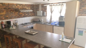 A kitchen with a granite countertop, wooden stools, a gas stove, a dishwasher, and a refrigerator. - Clanwilliam Accommodation (Cederberg)