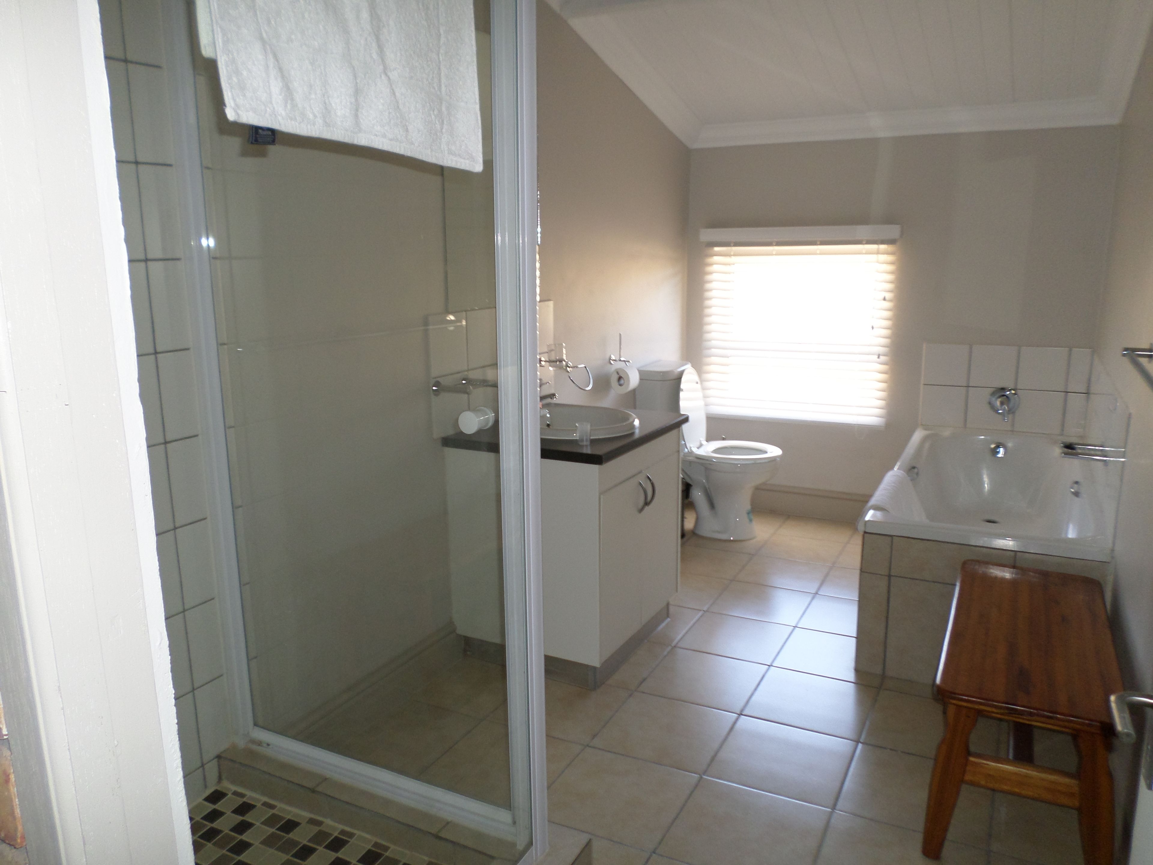 A bathroom with a glass-enclosed shower, a toilet, a sink, and a wooden stool.