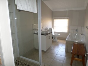 Un baño con ducha envuelta en vidrio, inodoro, lavamanos y un taburete de madera.