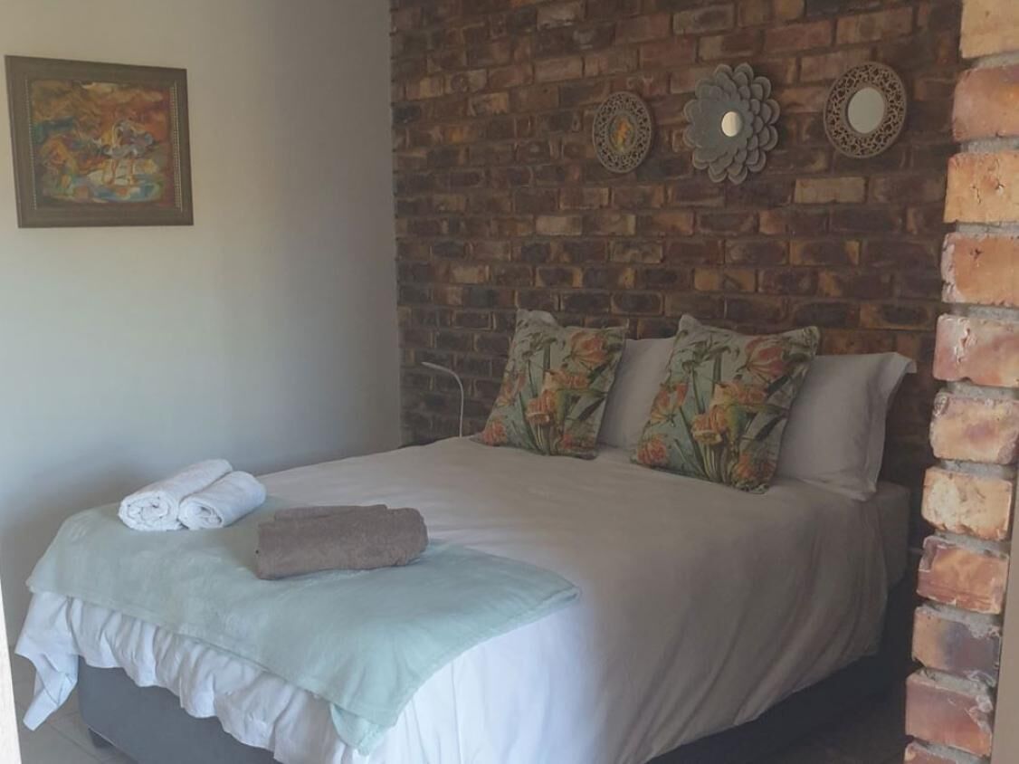 Una cama bien hecha con almohadas estampadas, un edredón blanco y toallas enrolladas a un lado.
