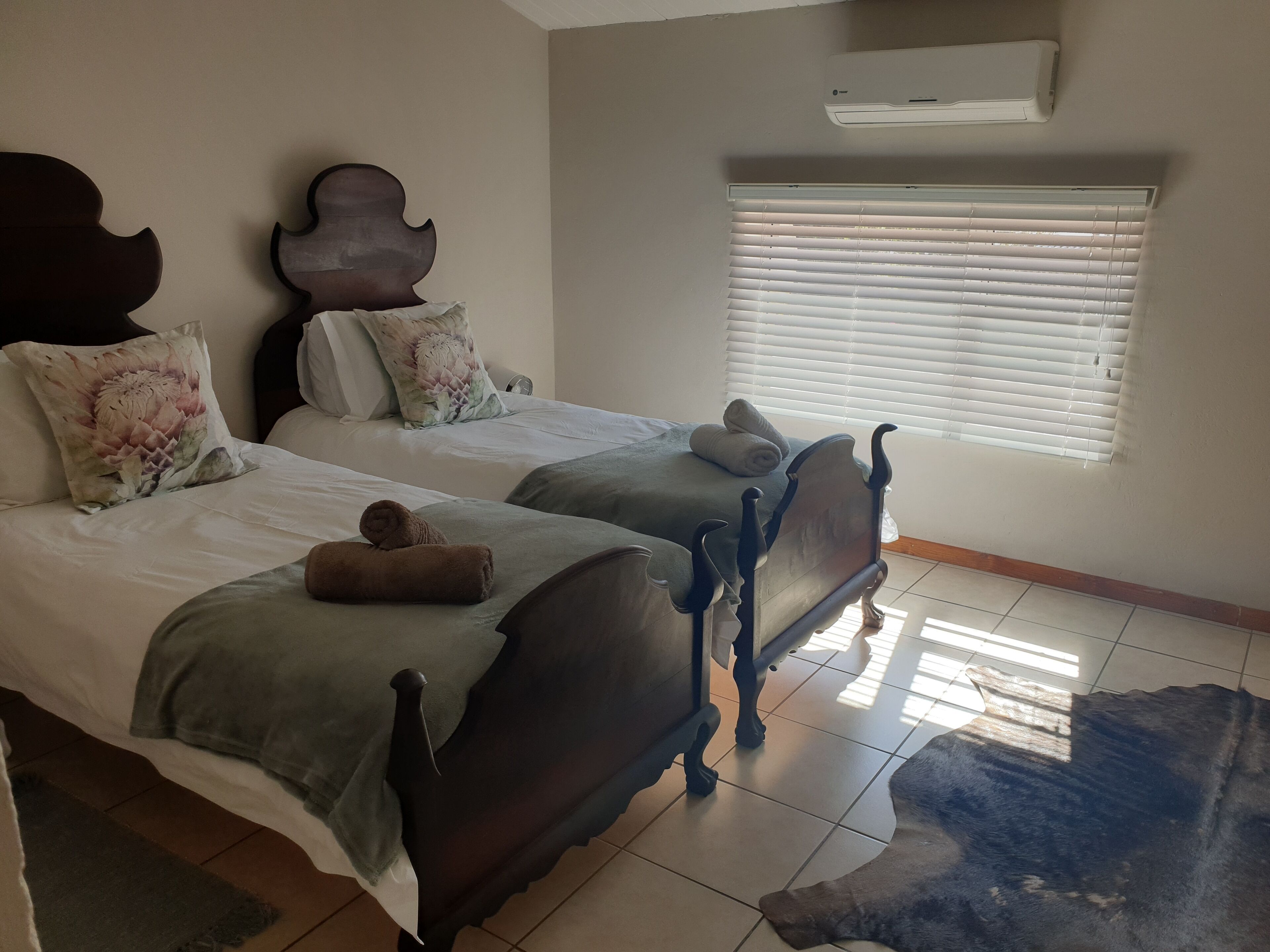 A bedroom with two beds, a window with blinds, an air conditioning unit, and a rug.
