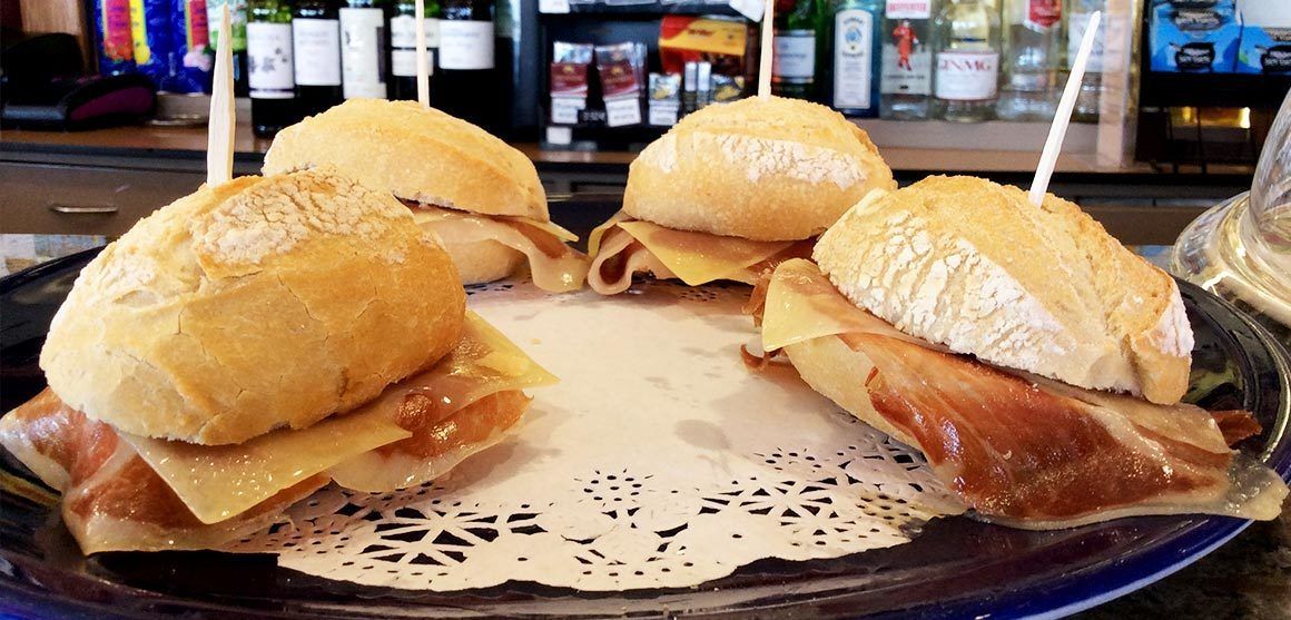 A plate with four sandwiches, each with a toothpick, on a doily.